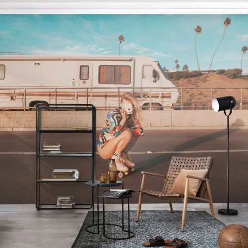 Fototapete Premium Sand - Ein Mädchen auf Rollschuhen mit einer Kamera vor einem Wohnmobil - 100x70cm - Lächel bitte! - Moderne Wanddekoration für Wohnzimmer und Schlafzimmer ARTTOR