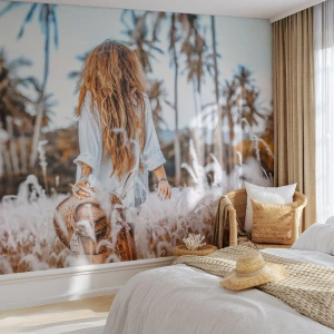 Fototapete Premium Canvas - Eine Frau auf einer Wiese mit Palmen im Hintergrund bei Sonnenuntergang - 100x70cm - Geboren aus Grasflaum - Moderne Wanddekoration für Wohnzimmer und Schlafzimmer ARTTOR