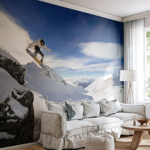 Fototapete Premium Canvas - Ein Snowboarder springt von einer Klippe mit schneebedeckten Bergen im Hintergrund. - 100x70cm - Freiheit ohne Grenzen - Moderne Wanddekoration für Wohnzimmer und Schlafzimmer ARTTOR