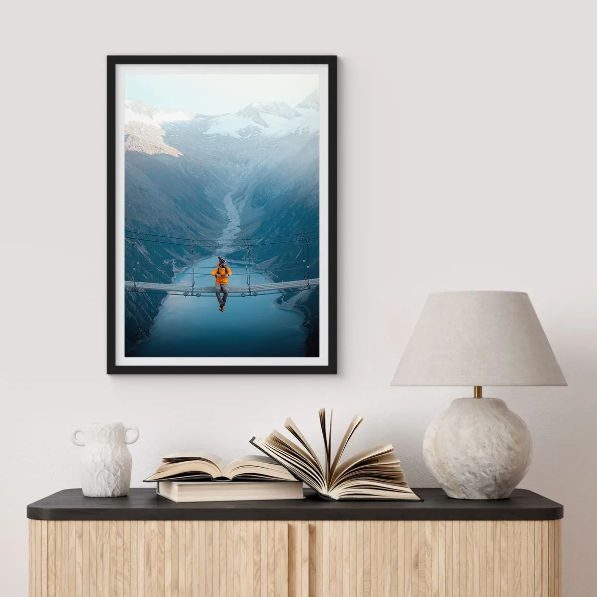 Poster in einem schwarzem Rahmen - Eine Person in einer gelben Jacke sitzt auf einer Hängebrücke über einem Tal - 50x70cm - Entzückt in der Schwebe - Moderne Wanddekoration für Wohnzimmer und Schlafzimmer ARTTOR