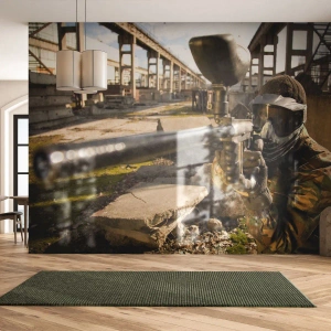 Fototapete Premium Sand - Ein Paintballspieler in Tarnkleidung zielt vor einer Ruinenkulisse - 100x70cm - Auch du kannst ein Held werden - Moderne Wanddekoration für Wohnzimmer und Schlafzimmer ARTTOR