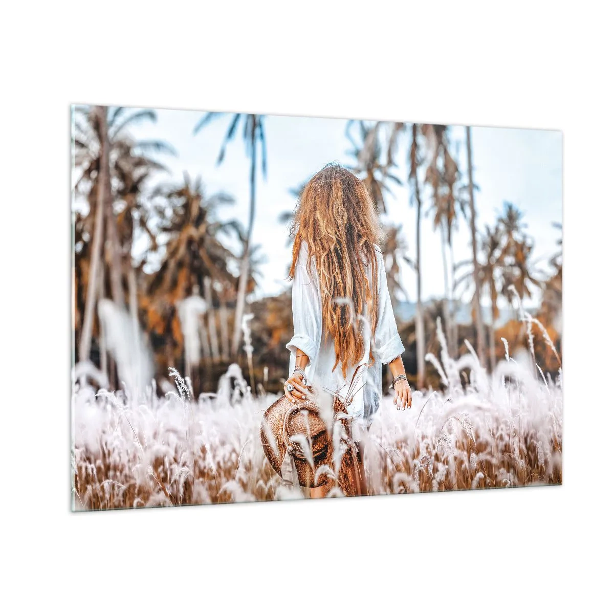 Glasbild - Bild auf glas - Eine Frau im Gras mit einem Hut in der Hand vor einem Hintergrund aus Palmen - 100x70cm - Geboren aus Grasflaum - Moderne Wanddekoration für Wohnzimmer und Schlafzimmer ARTTOR